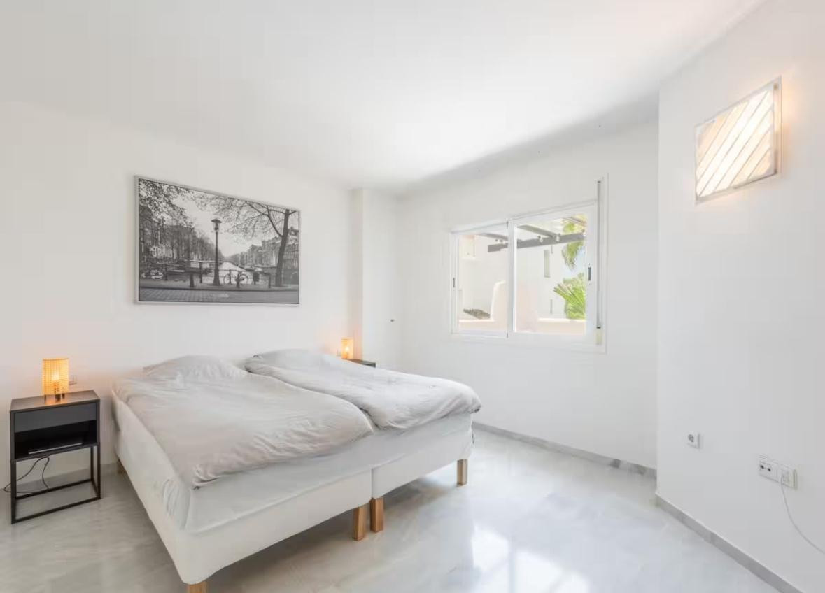 Bedroom featuring two single beds, a large window, black nightstands, and a black and white cityscape artwork.