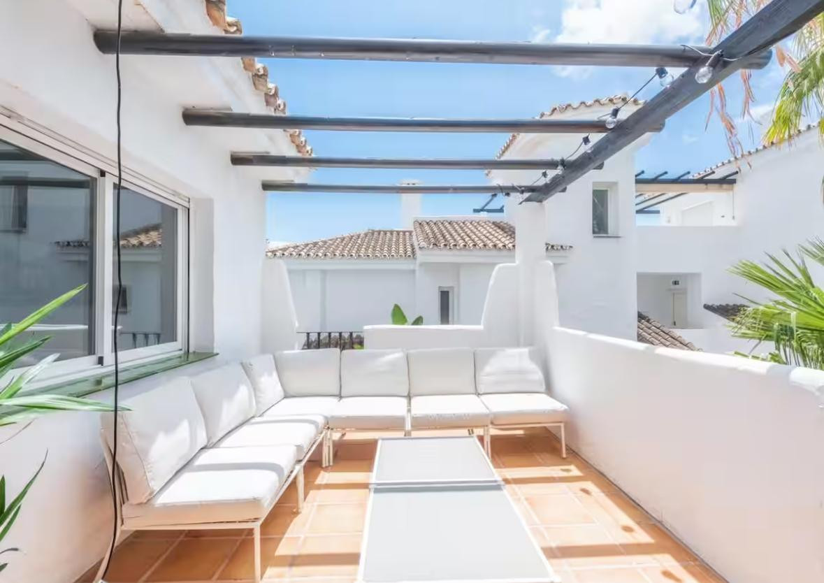 Rooftop terrace featuring a white sectional sofa, coffee table, and an open pergola.