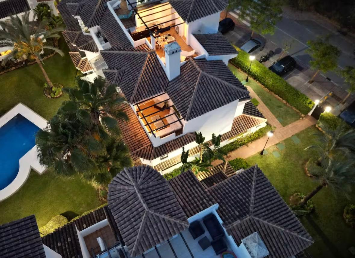 Aerial view of tiled rooftops, illuminated courtyards, a pool, and streetlights at dusk.
