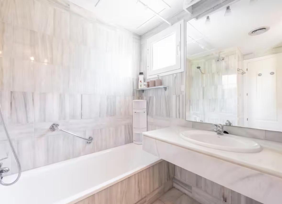 Bathroom with white and gray marble tiles, a bathtub with shower head, and a vanity with a large mirror.