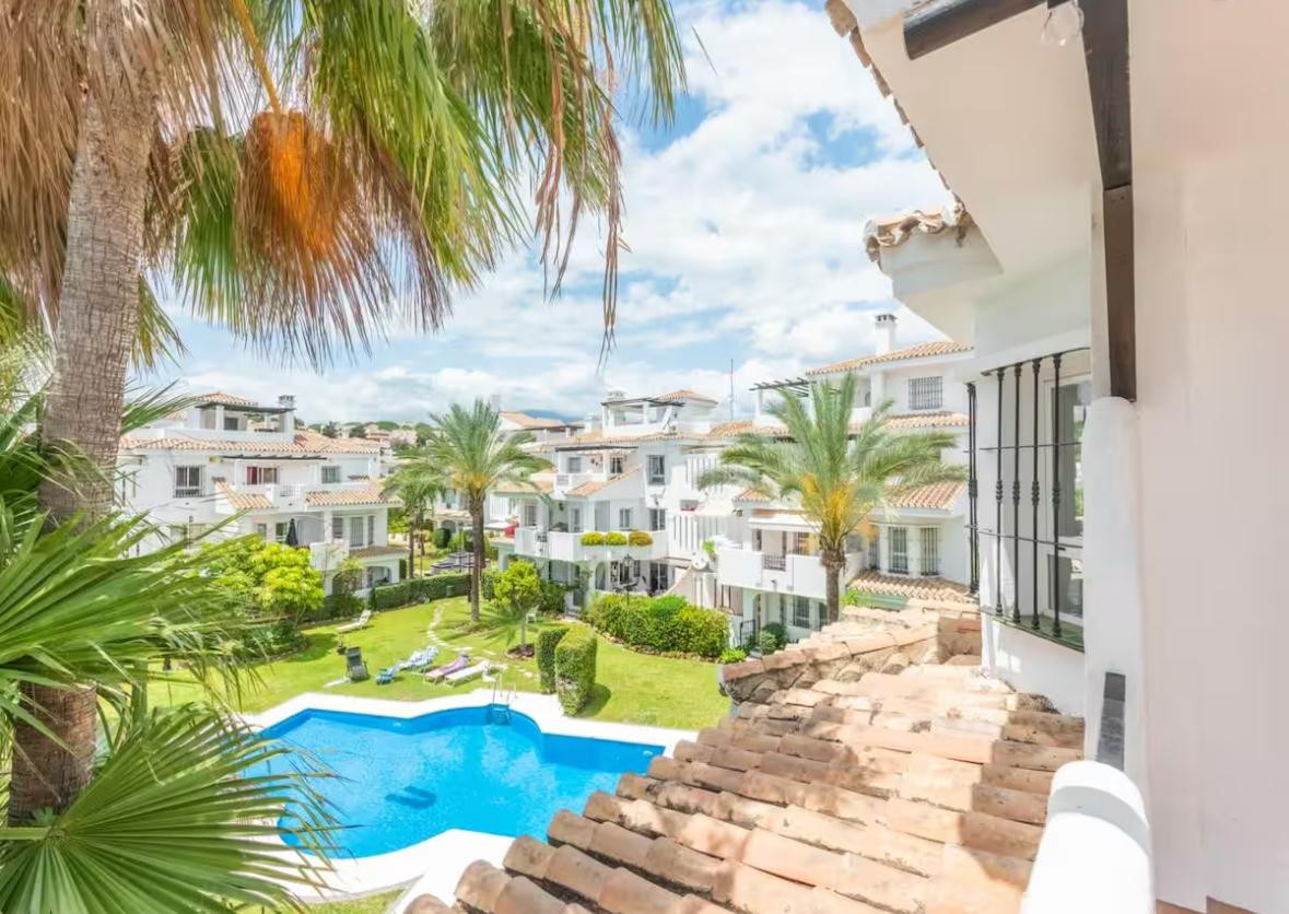 Aerial view of a residential complex with a swimming pool, green lawn, and palm trees.