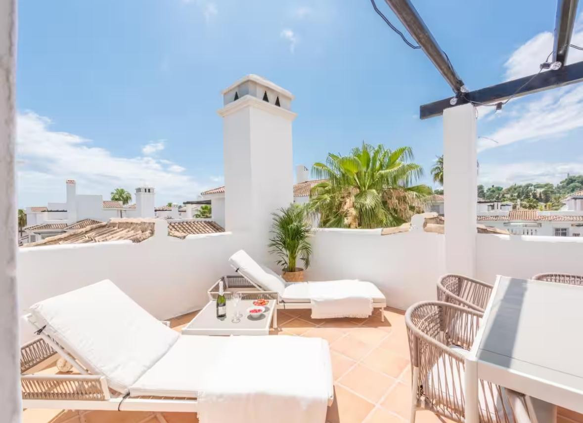 Close up of a rooftop terrace with lounge chairs, a small table with champagne, and a plant.