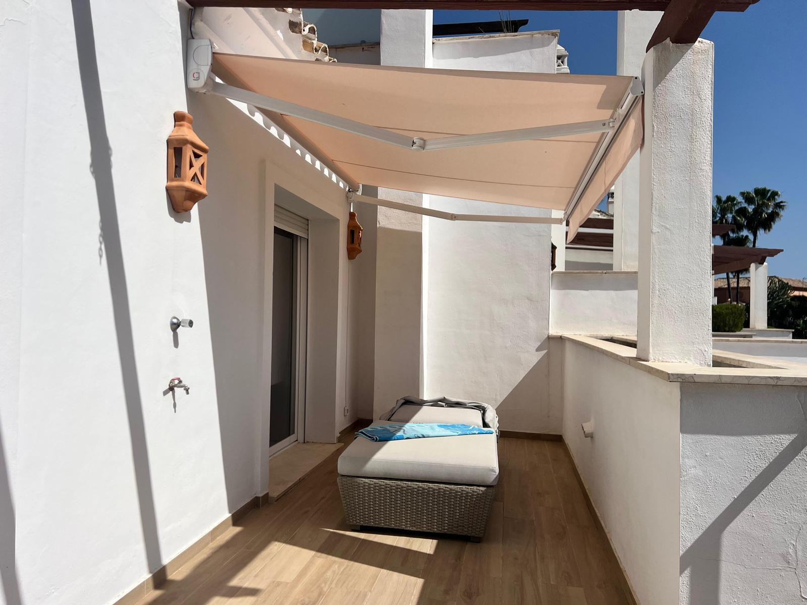 Exterior terrace with a sun lounger, retractable awning, terracotta wall lights, and white stucco walls.