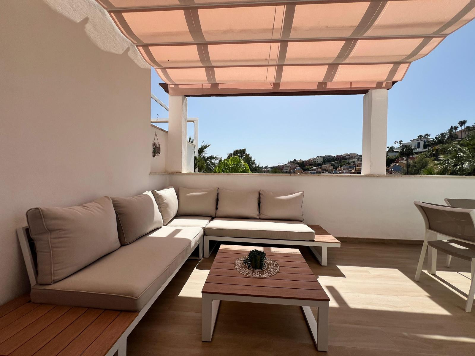 Outdoor L-shaped sofa seating area on a terrace, with a low wooden coffee table and town view.