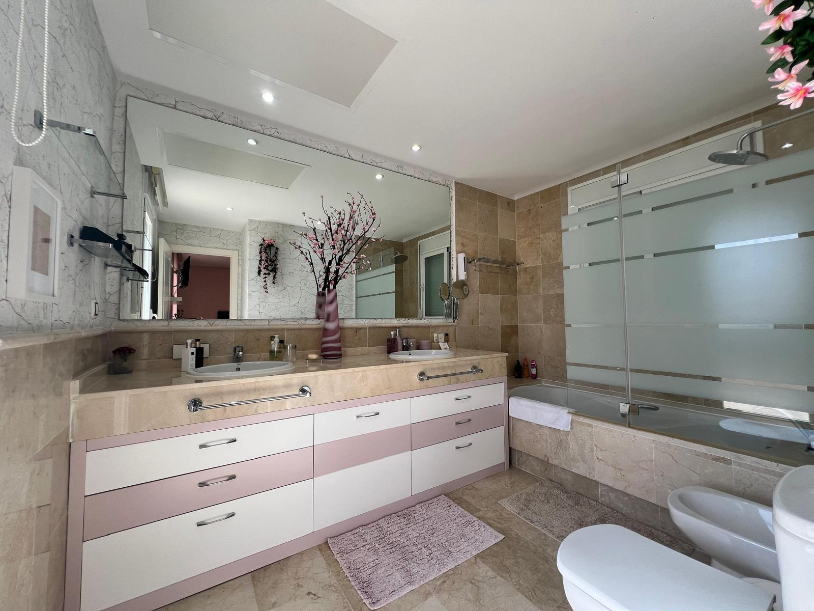 Bathroom with double vanity, large mirror, tiled walls, bathtub with shower, and toilet with bidet.