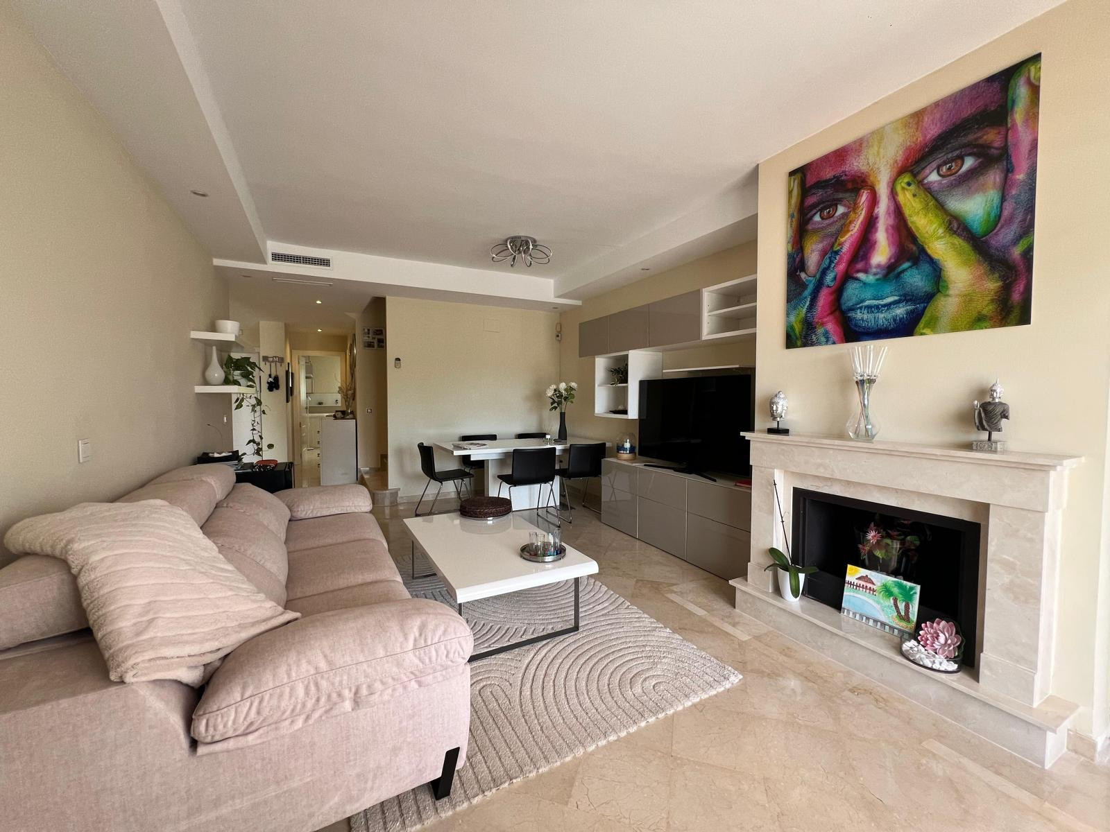 Living room with light sofa, coffee table, colorful art above a fireplace, and a television unit.