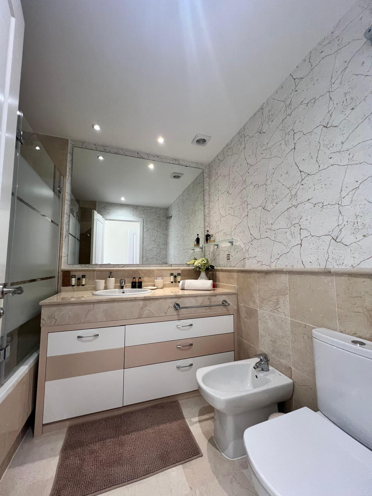Bathroom with a large vanity mirror, single sink, toilet, bidet, and patterned accent wall.