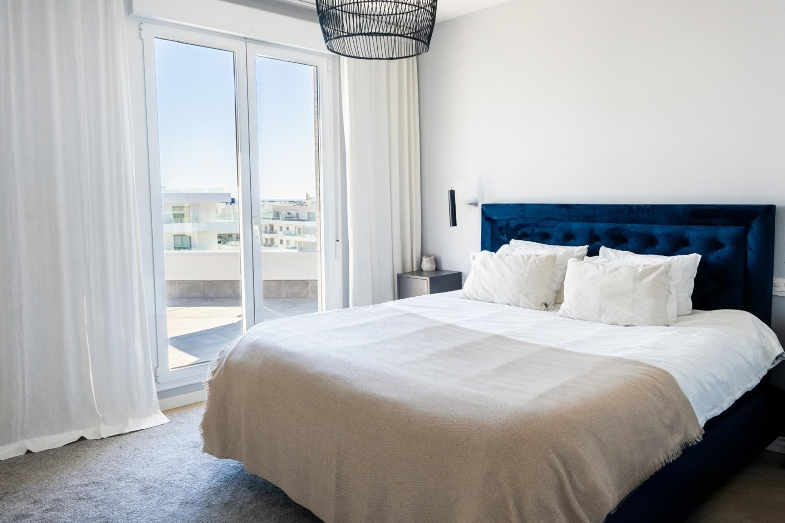 Bedroom with a blue velvet bed, a large glass door leading to a terrace, and a black pendant light.