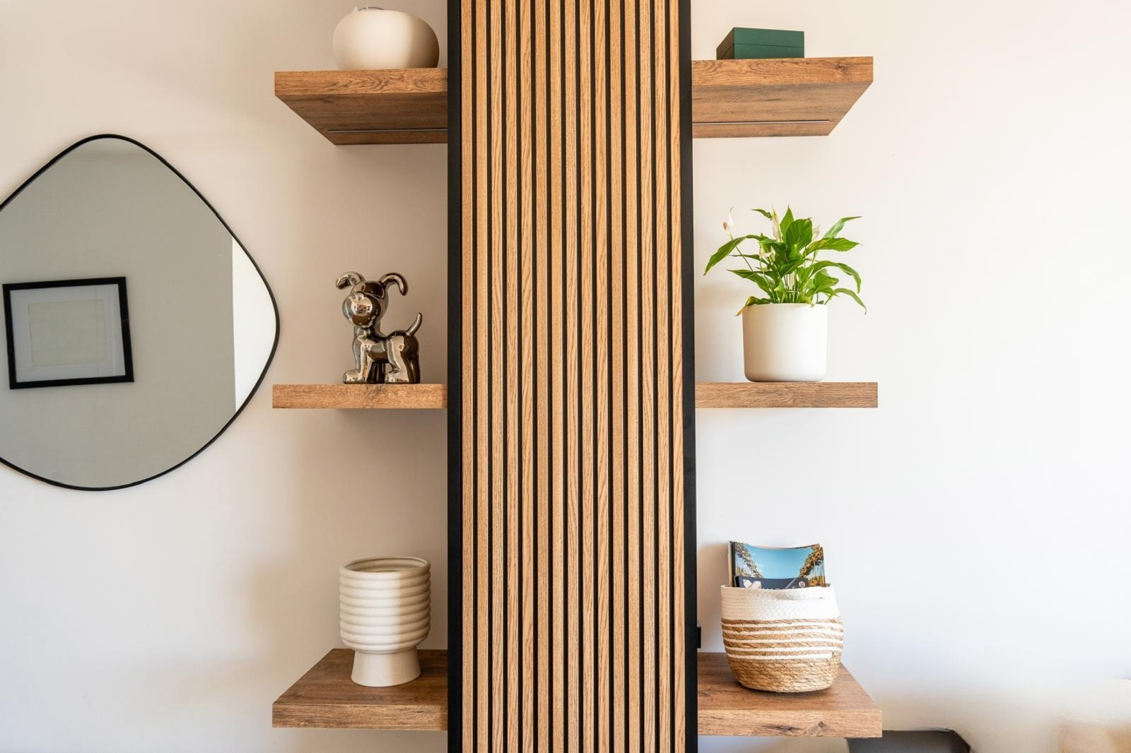 Close up of decorative wooden shelves with a plant, abstract dog statue, and an irregular shaped mirror.