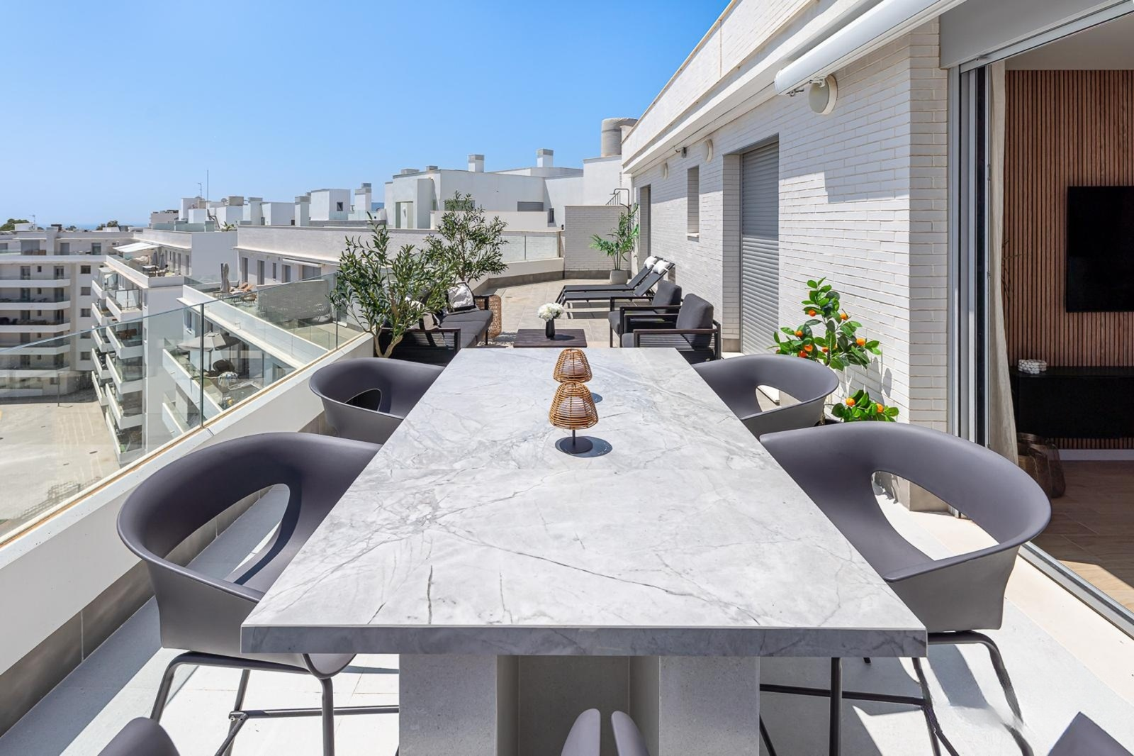 View of the expansive rooftop terrace featuring a dining table, lounge chairs, and city rooftops.