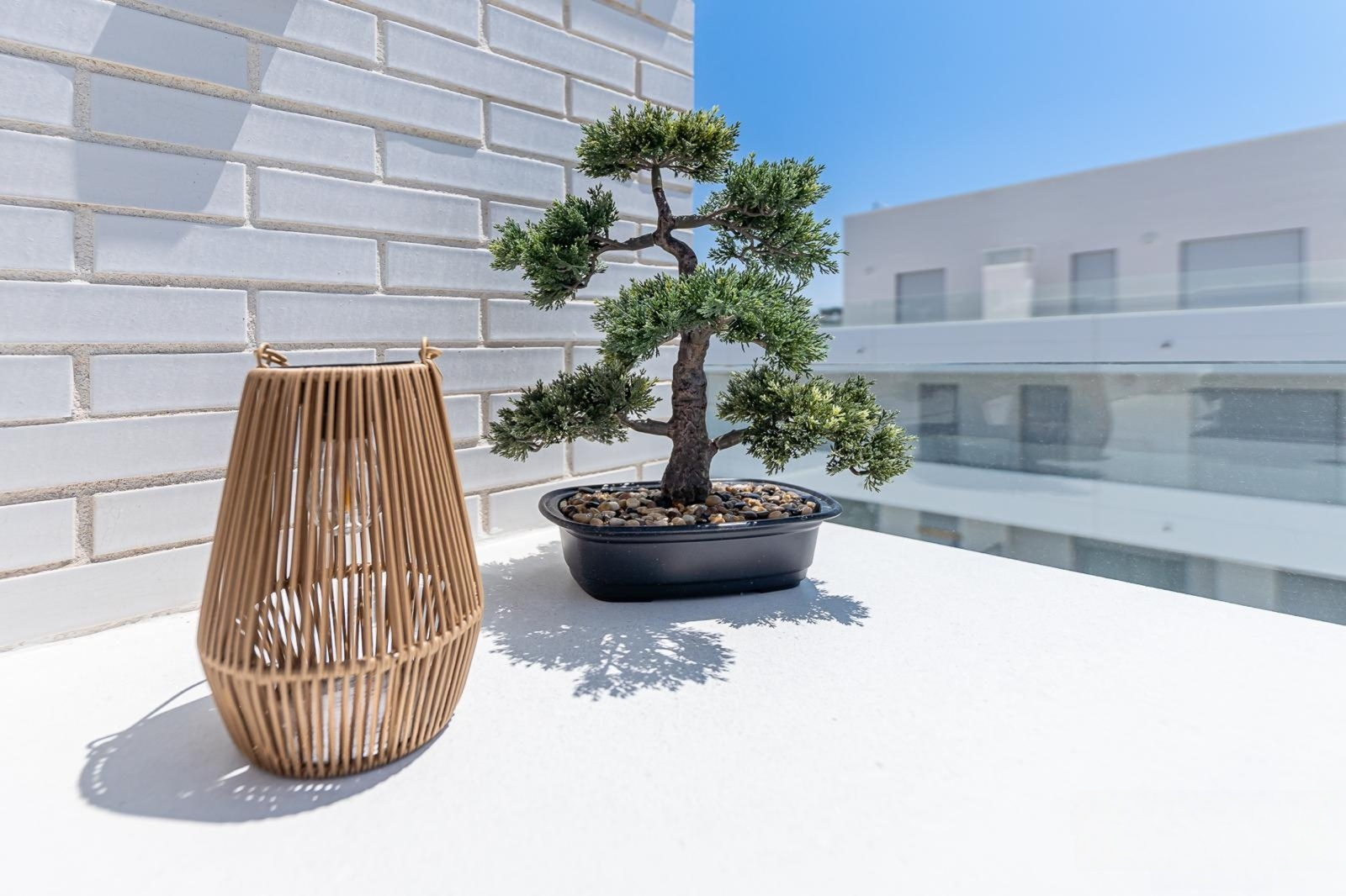 Close up of a decorative bonsai tree and a woven lantern on a white balcony ledge.