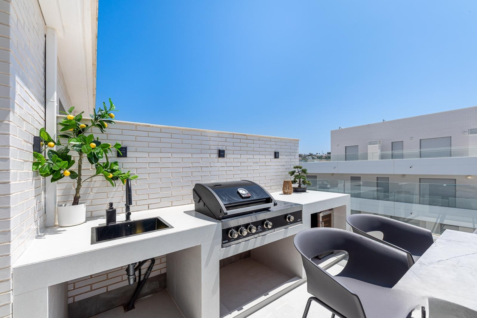 Close up of an outdoor kitchen area with a built-in grill, sink, and white brick wall.