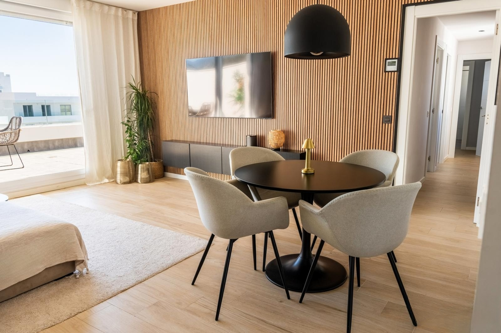 Living room with a large TV on a slatted wood wall, dining table, and floor to ceiling windows.