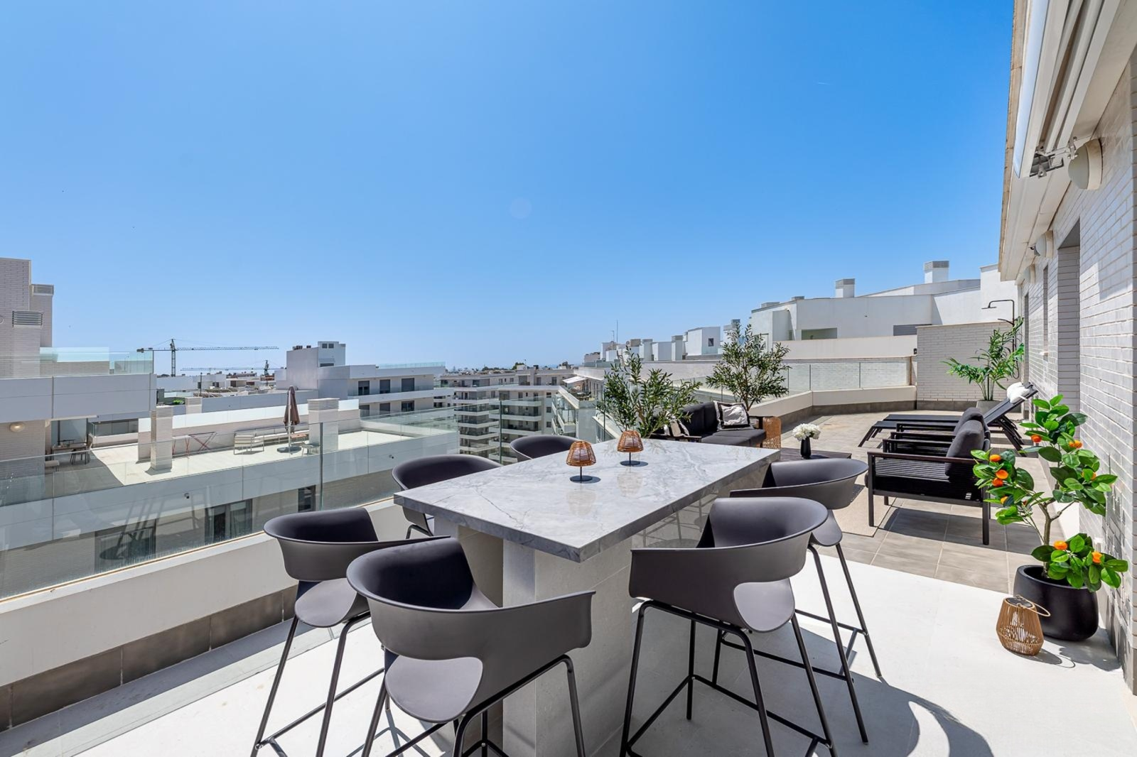 Rooftop terrace with a large marble bar table and stools overlooking distant city and ocean.