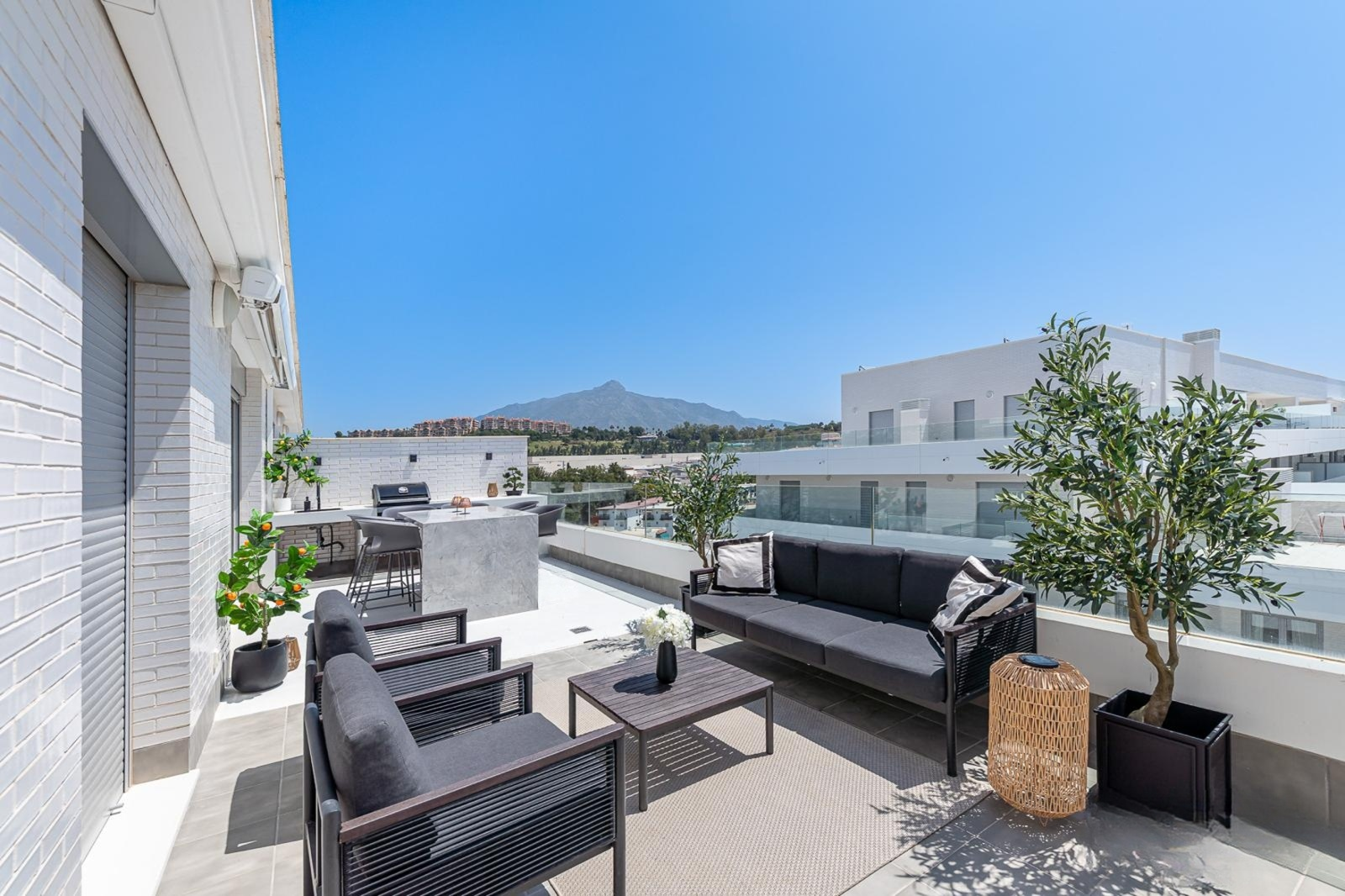 Rooftop terrace with outdoor lounge seating and a built in barbecue area, distant mountains.