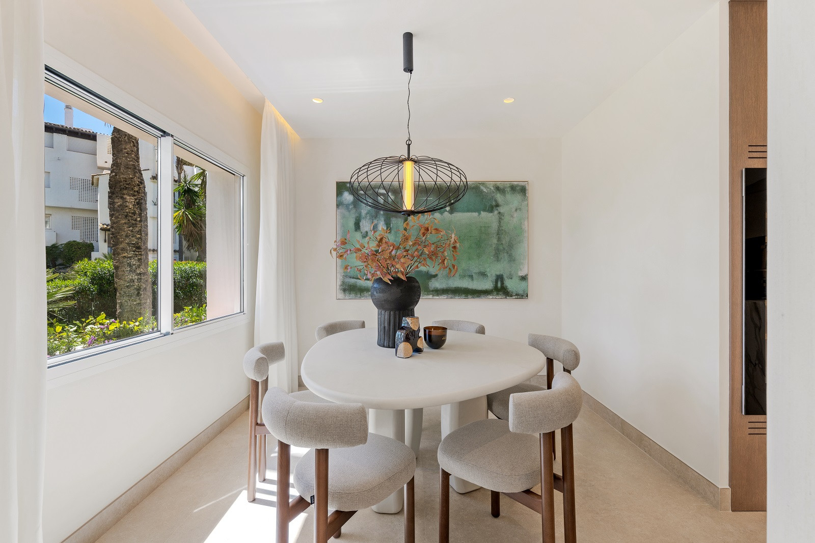 Straight-on view of the dining area with a round white table, pendant light, and small window.