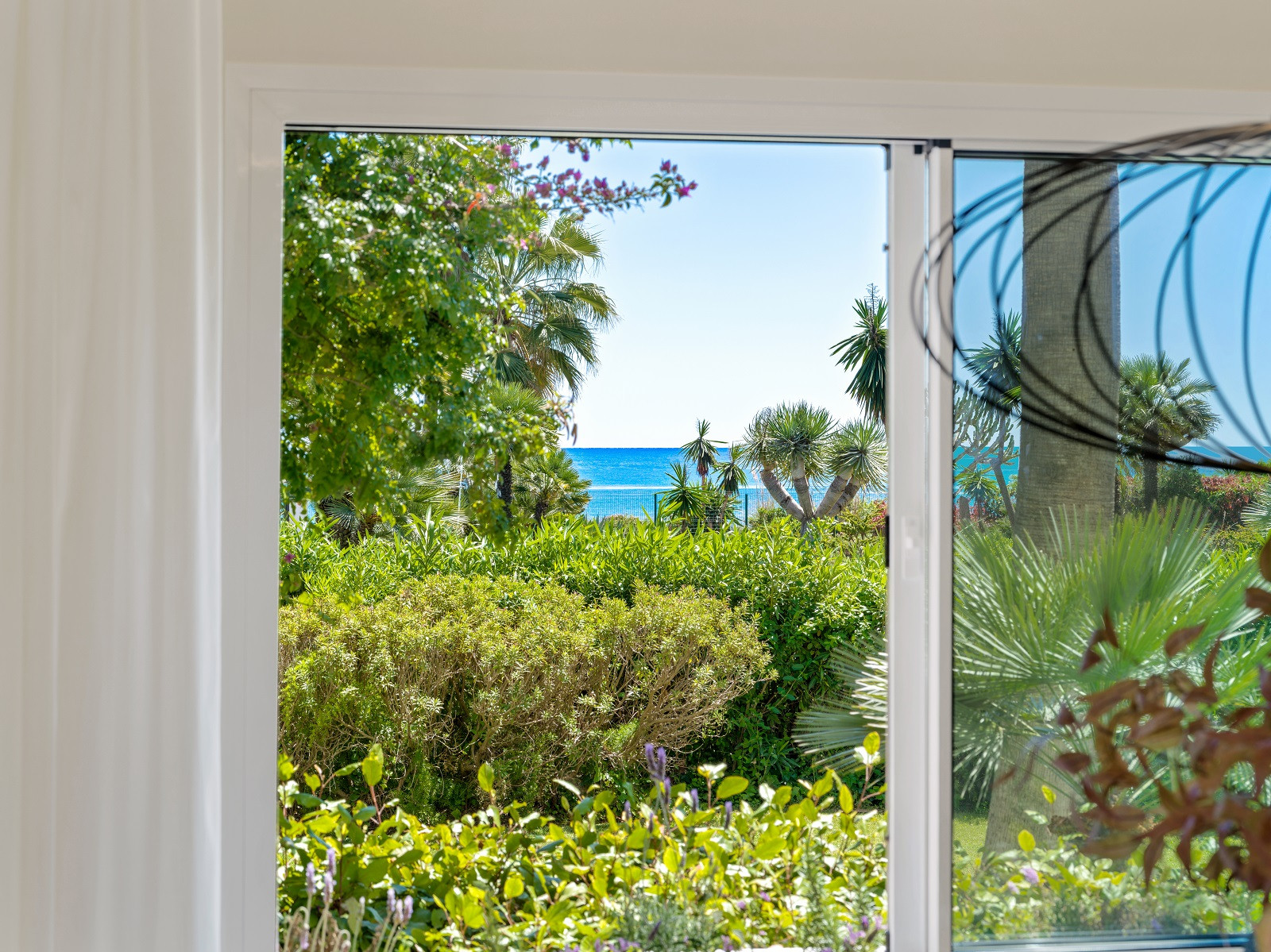 Close-up of a window with a view of a green garden and the blue ocean beyond.