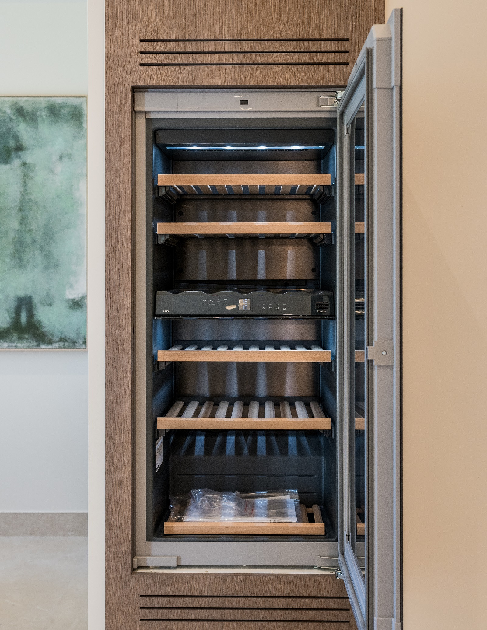 Built-in wine cooler with a glass door slightly ajar, showing empty wooden shelves and internal lighting.