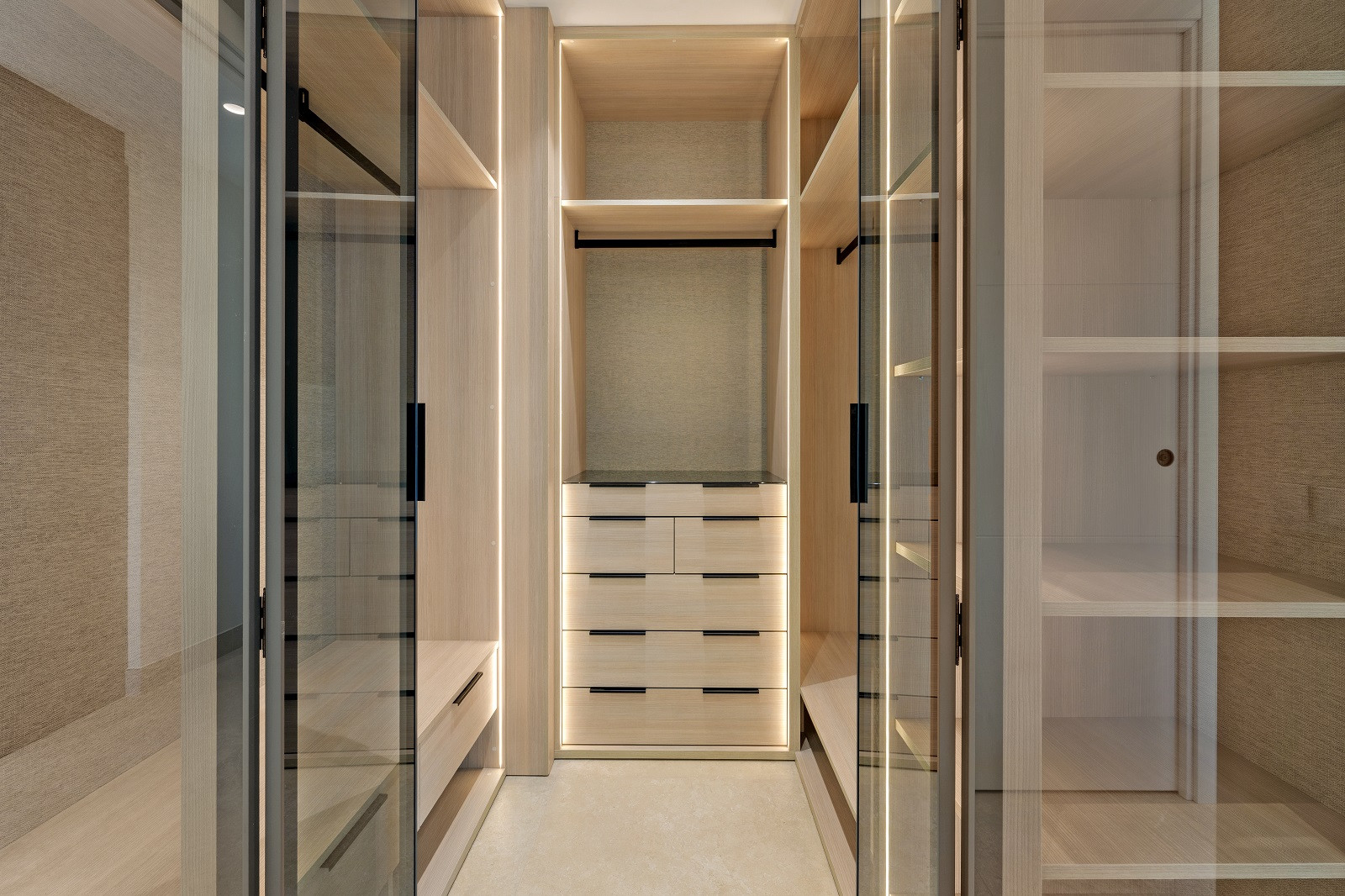 Walk-in closet with light wood shelving, drawers, and glass-fronted cabinets with integrated lighting.