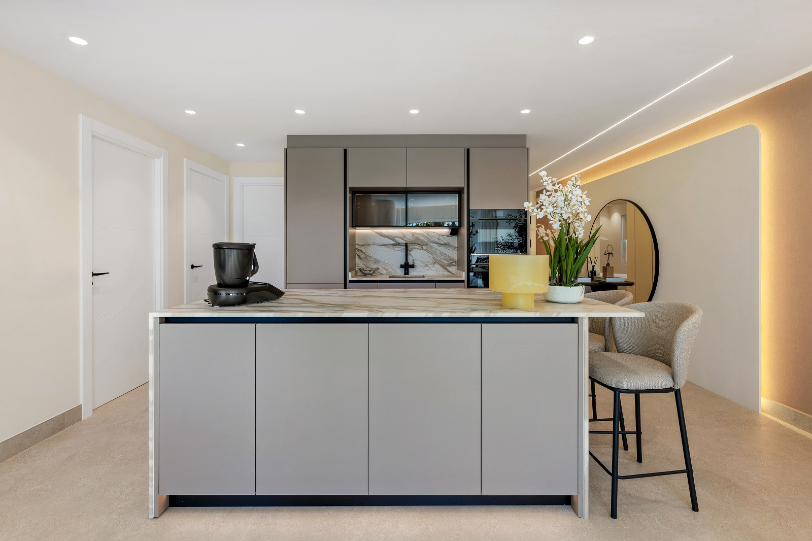 View of a contemporary kitchen with a large island from the front, showing bar stools and integrated ovens.
