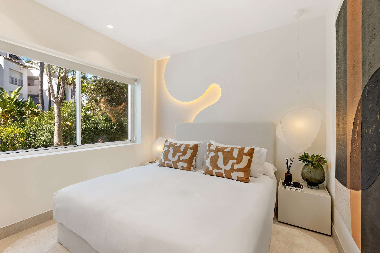 Bedroom with a large window overlooking lush greenery and a decorative wall light feature.