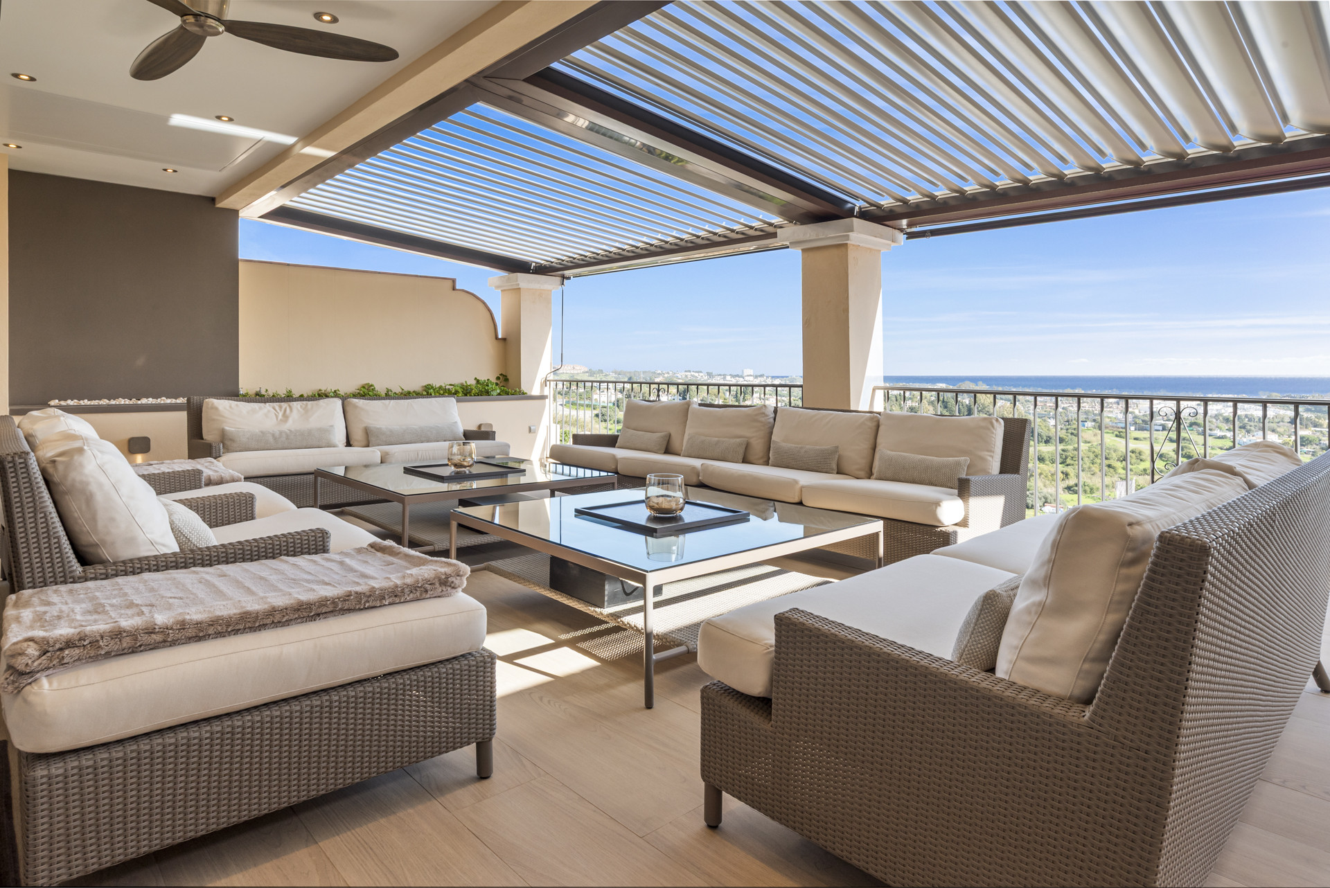 Outdoor patio with multiple seating areas under a louvered pergola and sea view.