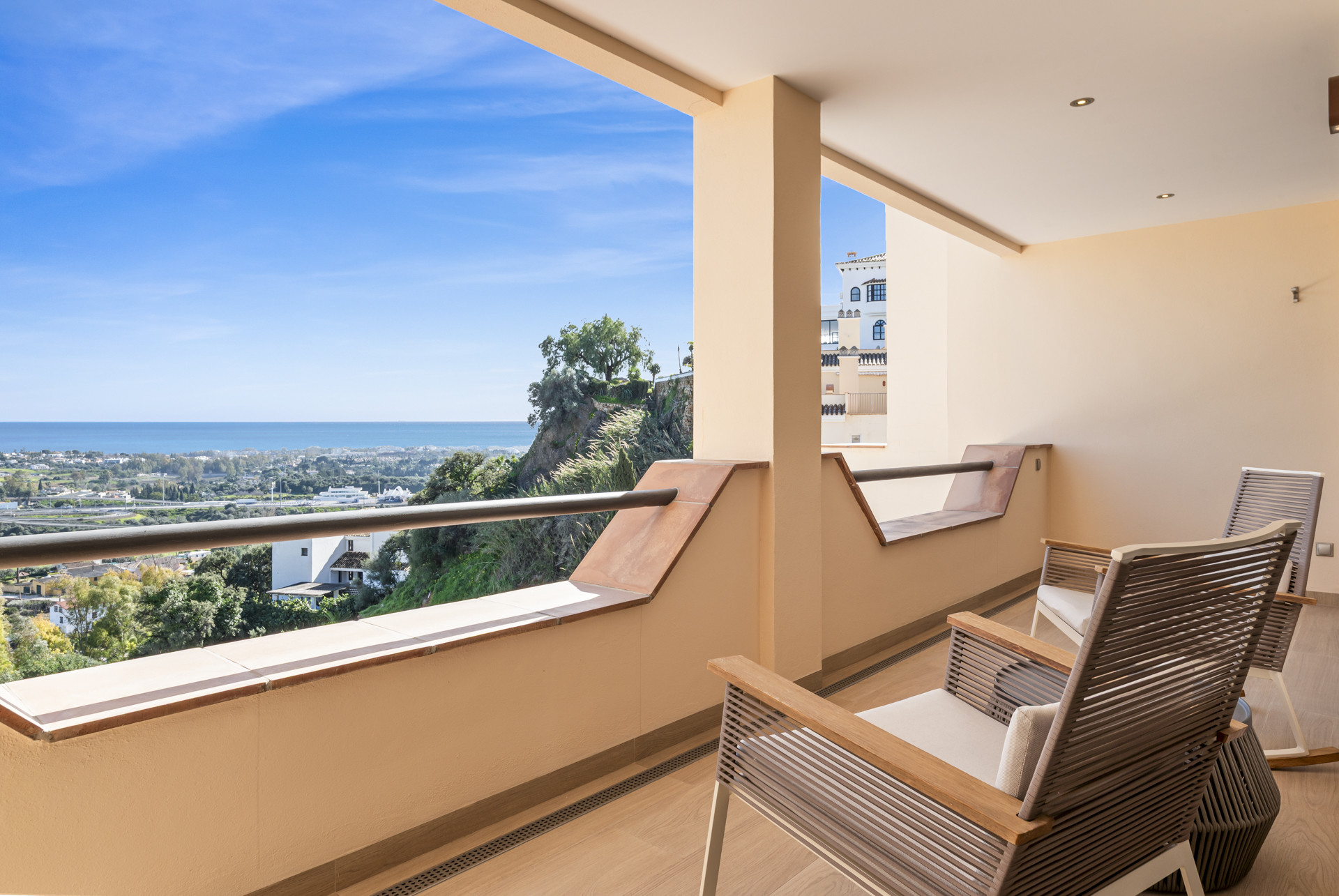 Outdoor balcony with four modern chairs facing a panoramic view of the sea and surrounding town.