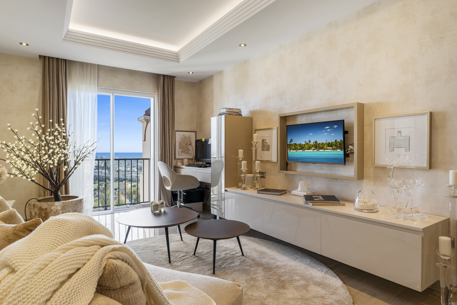 Living room with a mounted TV, white media console, desk, and balcony access.
