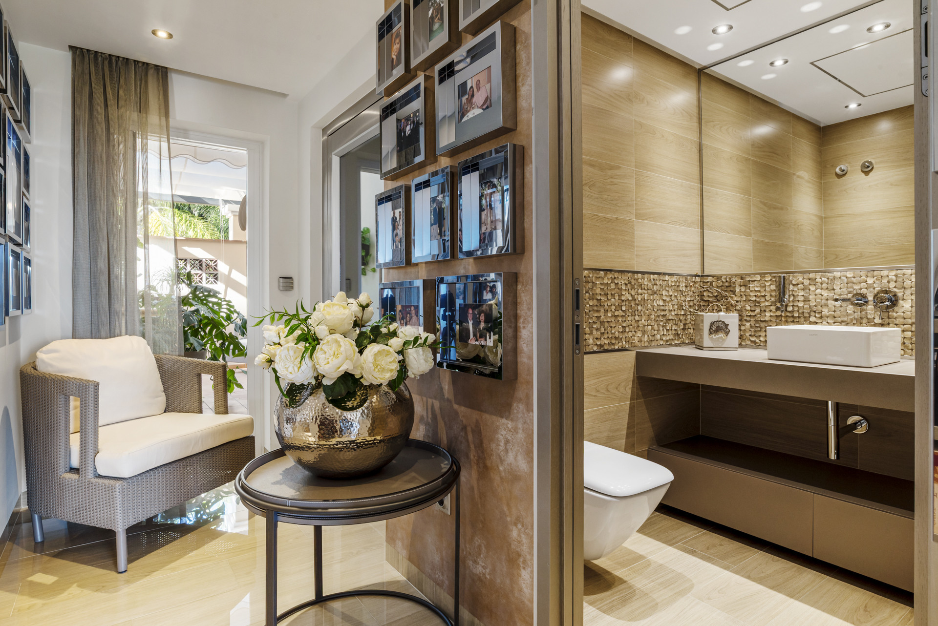 Entryway with flower arrangement and a view into a modern bathroom with wood-look tiles.