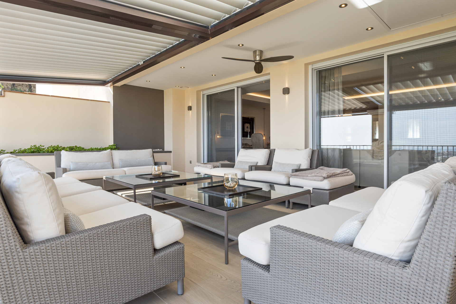 Outdoor covered patio with modern furniture, ceiling fan, and sliding glass doors.
