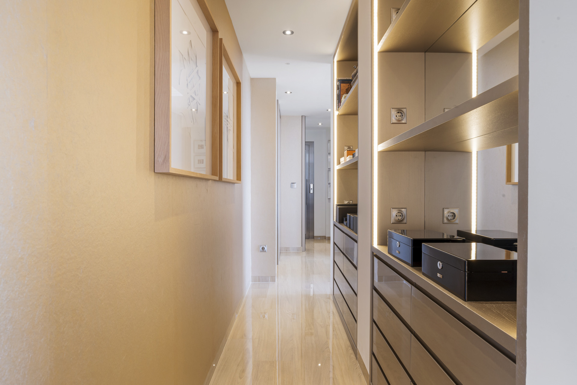 View of a brightly lit hallway with a long closet on the right and framed art on the left wall.
