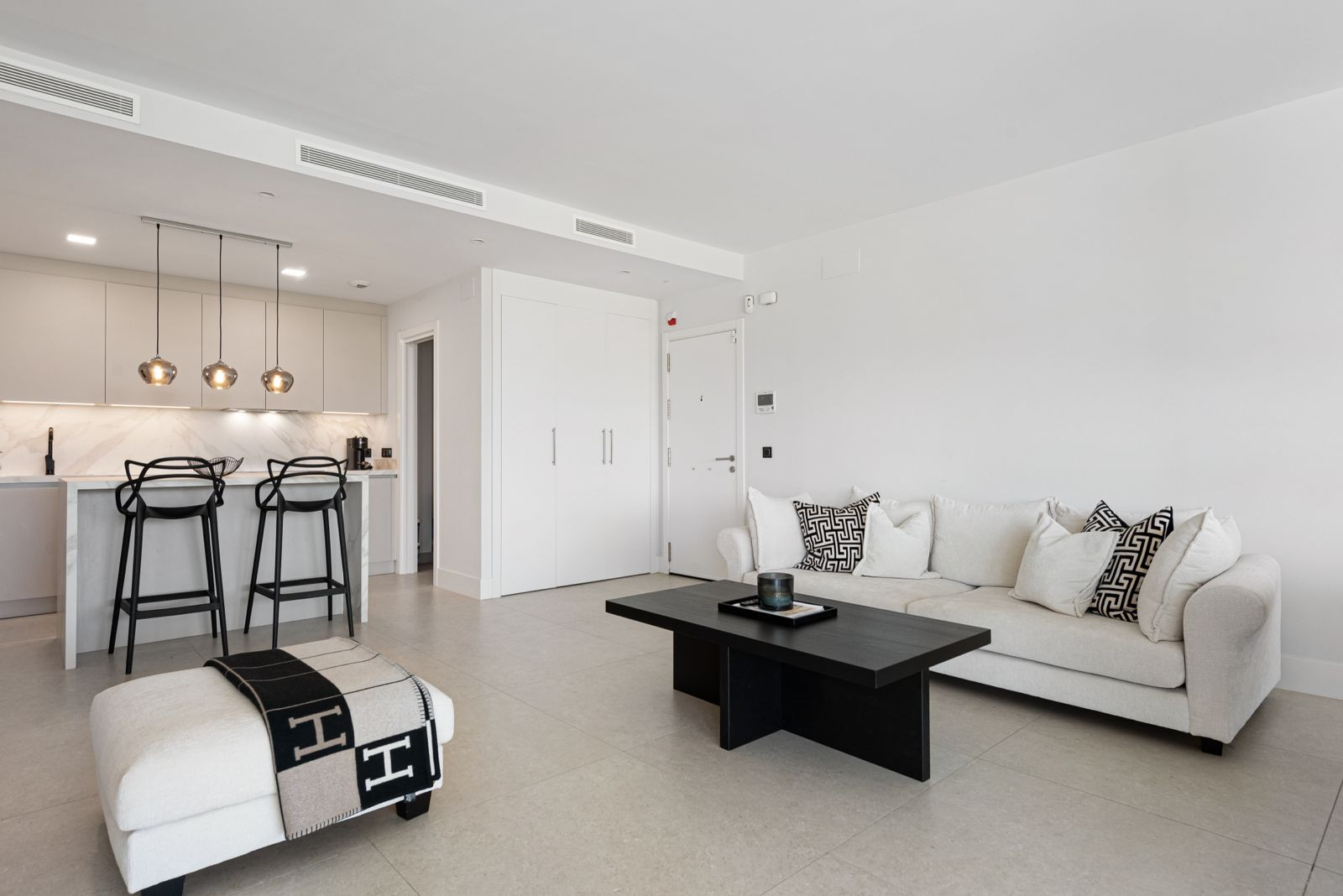Open plan living room with white sofa and dark coffee table, adjacent to a modern kitchen island with bar stools.