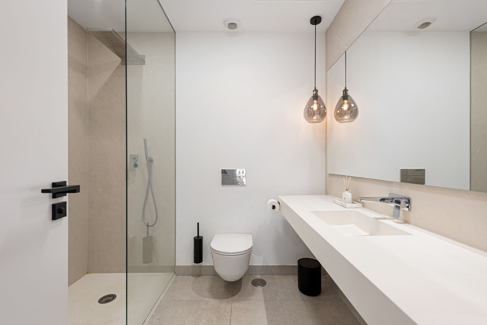 Contemporary bathroom with a floating vanity, two pendant lights, a wall-mounted toilet, and a glass shower.
