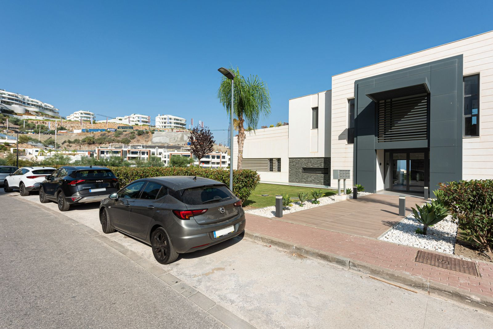 Exterior of a modern building with parked cars on the street and a paved walkway leading to the entrance.
