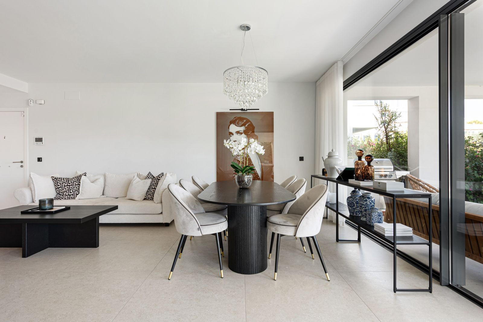 Open plan living and dining area with a white sofa, dark dining table, chandelier, and sliding glass doors to patio.