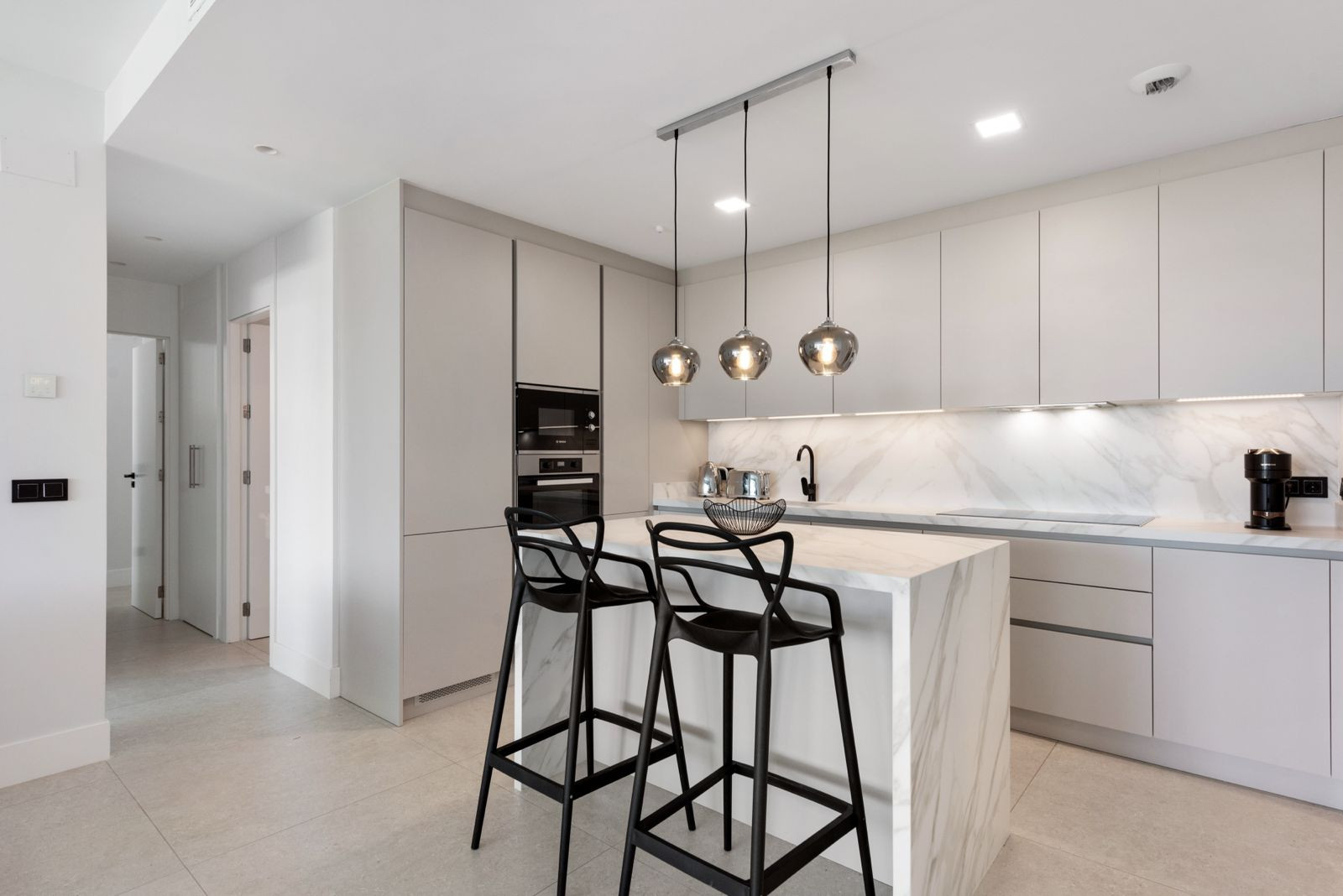 Modern kitchen with light grey cabinets, a marble island with two bar stools, and pendant lighting fixtures.