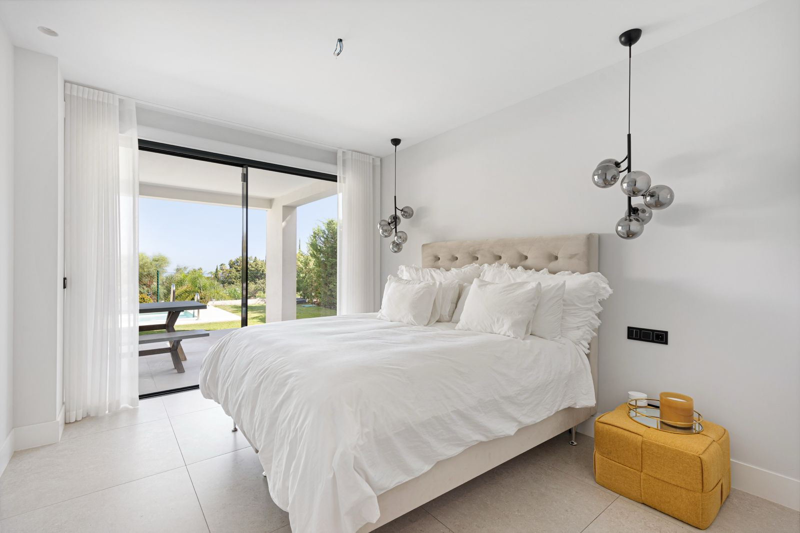 Bedroom with a large white bed, two hanging light fixtures, and glass sliding doors leading to an outdoor area.