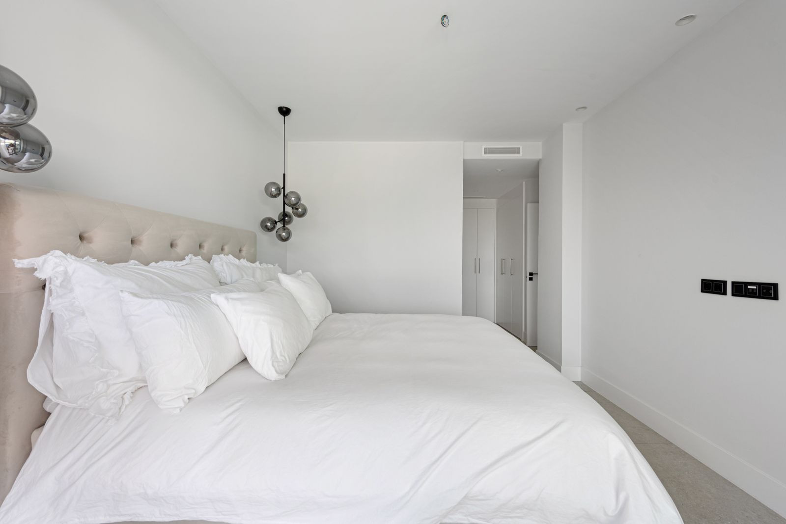 Bedroom with a large white bed, a single hanging light fixture, and an open doorway leading to a walk-in closet.
