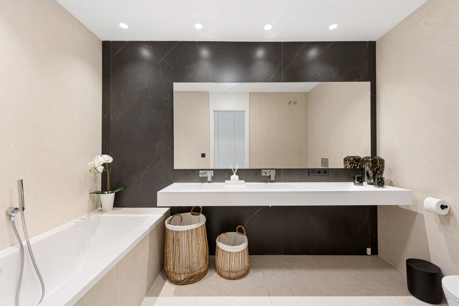Bathroom with dual white sinks set against dark marble, a large mirror, and a freestanding bathtub to the left.
