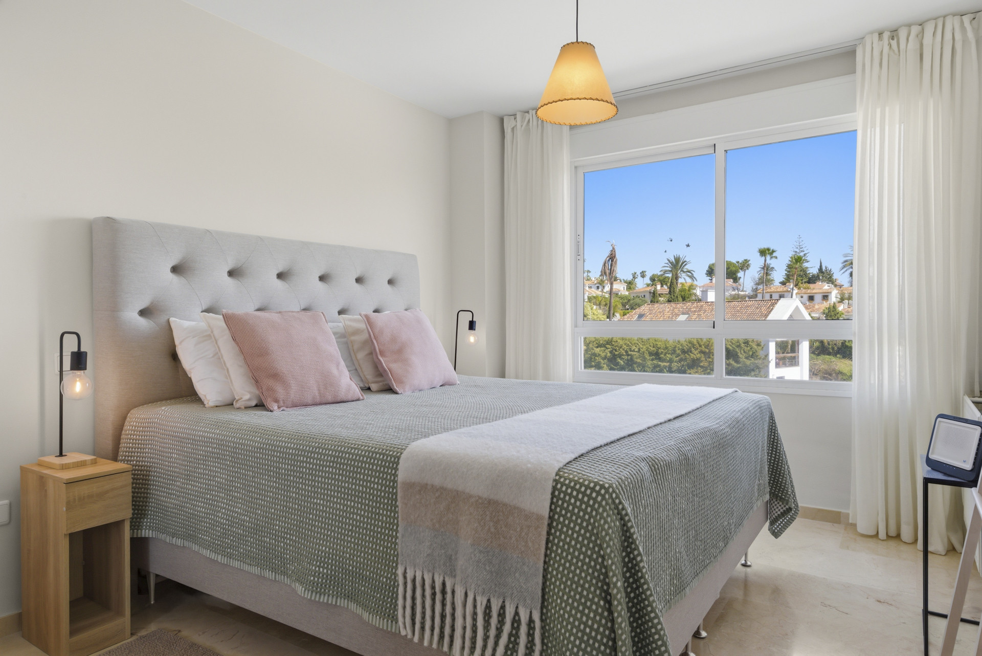 Bright bedroom with a gray upholstered headboard and large window overlooking palm trees.