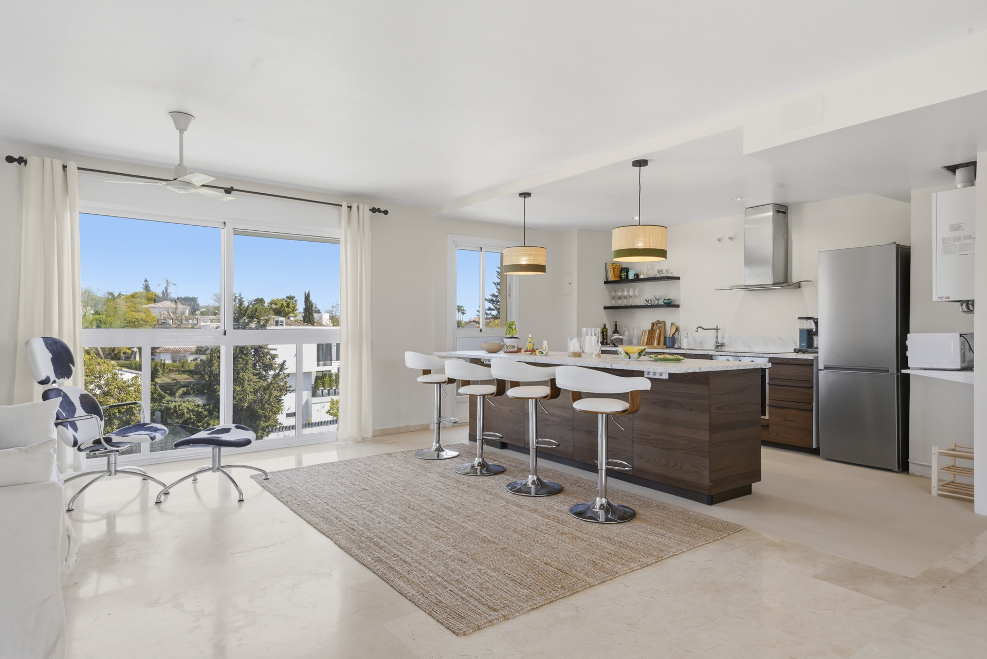 Bright kitchen area showcasing bar stools and large windows with floral views.