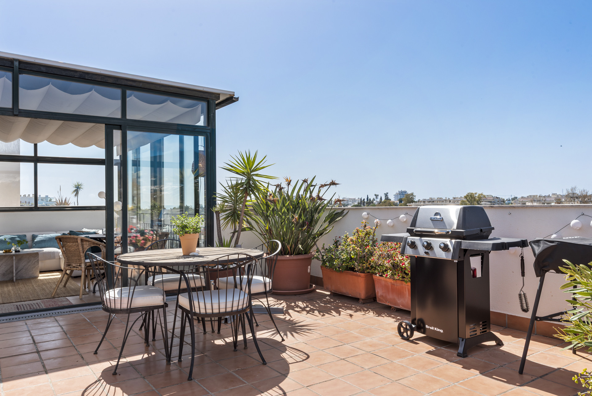 Glass-enclosed patio area adjoining terrace with dining set and barbecue grill.