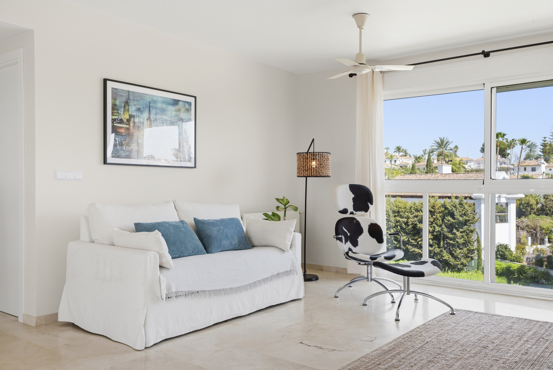 Seating area with a white sofa and a patterned chair beside a window view