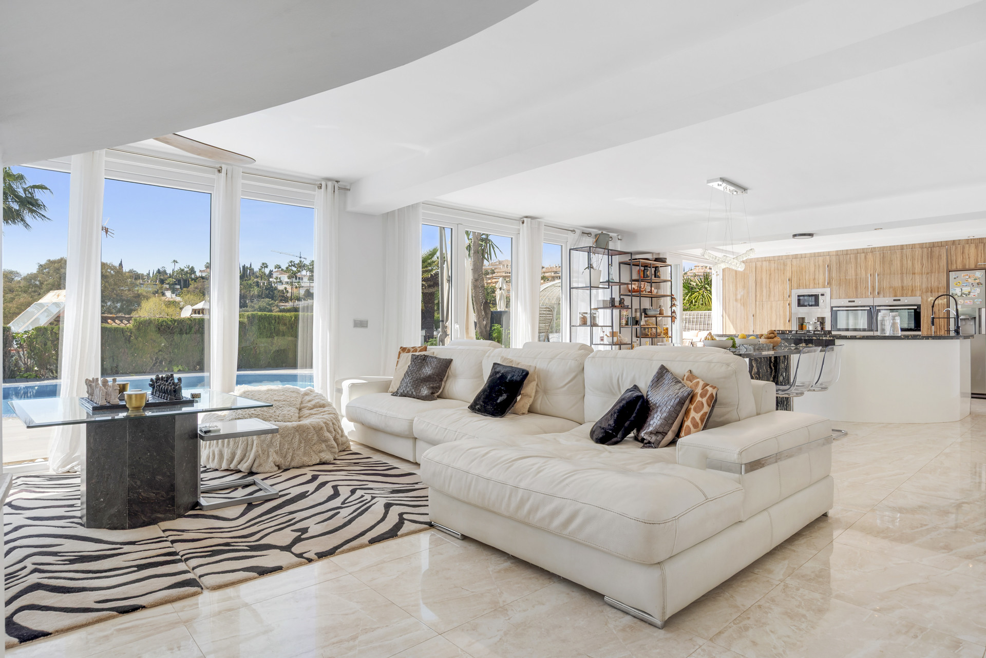 White living room with large sectional sofa, zebra rug, glass coffee table, and patio view.