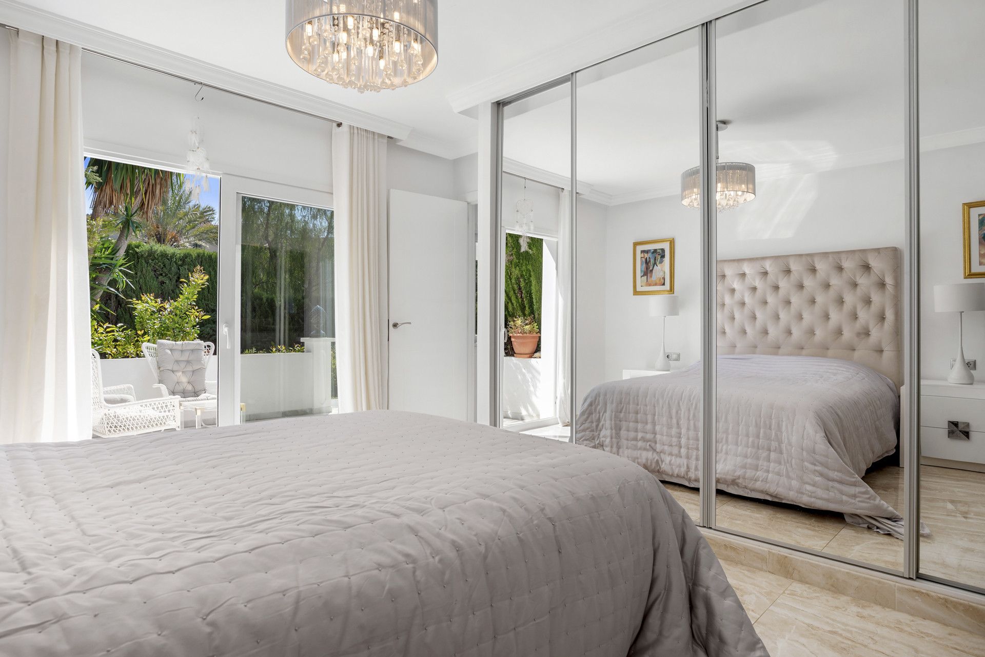 Bedroom with a bed, mirrored wardrobes, a chandelier, and balcony access with white curtains.