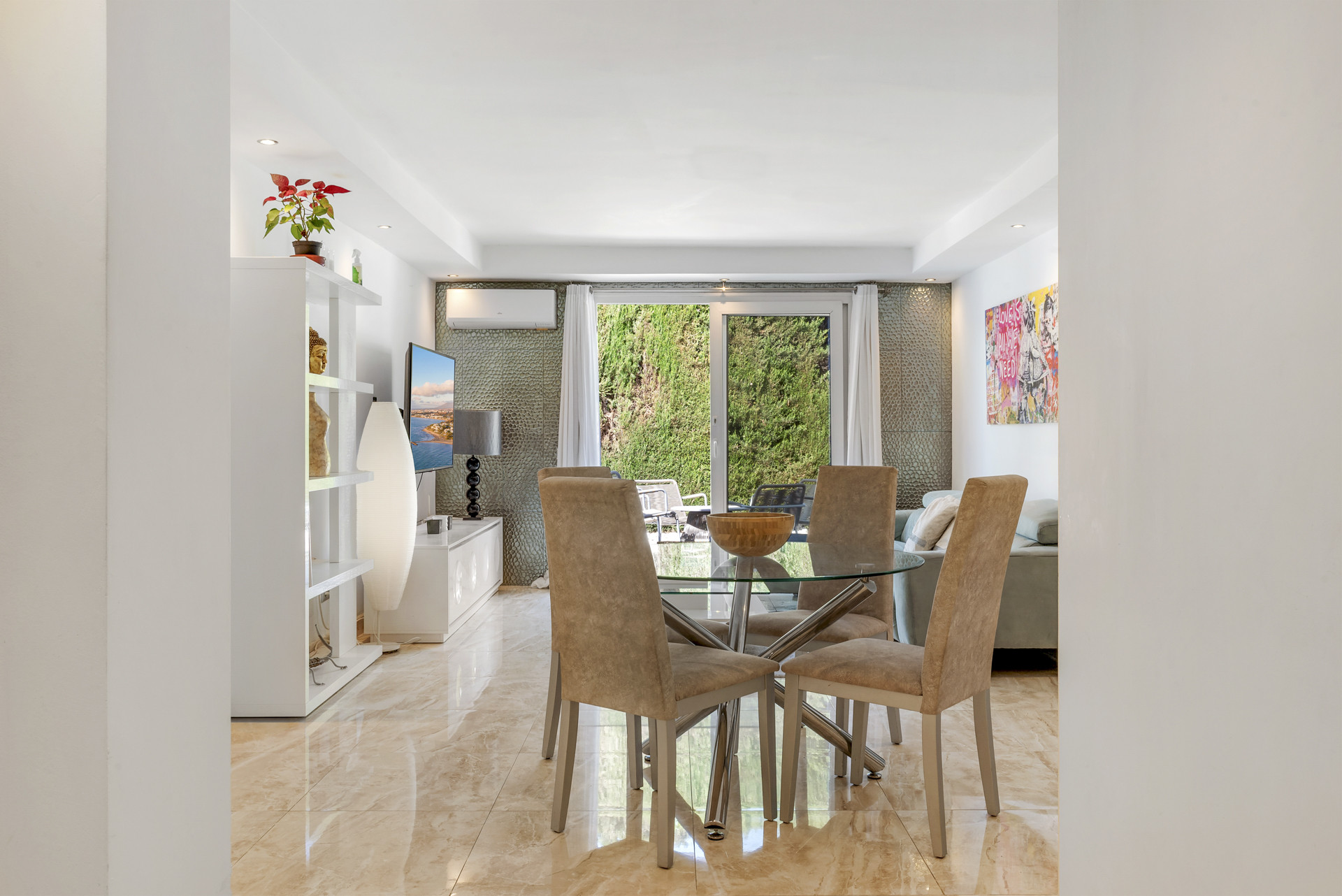 Dining area with a glass table and four chairs, visible living room, and sliding doors to a patio.