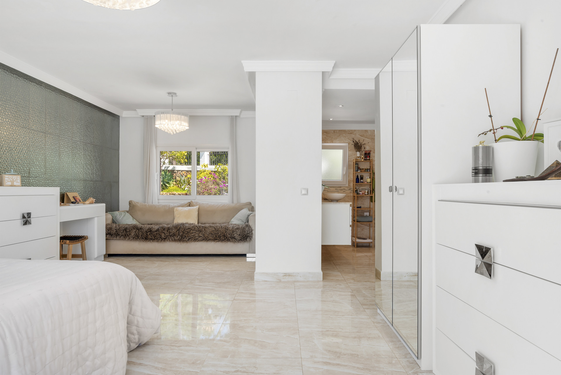Bedroom suite showing a bed, white dresser, mirrored wardrobe, and a sofa in an adjacent sitting area.