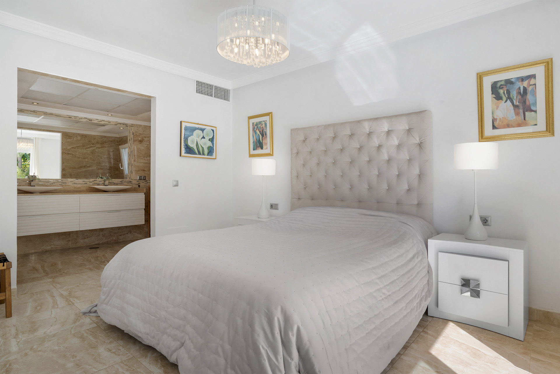 Bedroom with a tufted headboard bed and an en suite bathroom featuring dual sinks.
