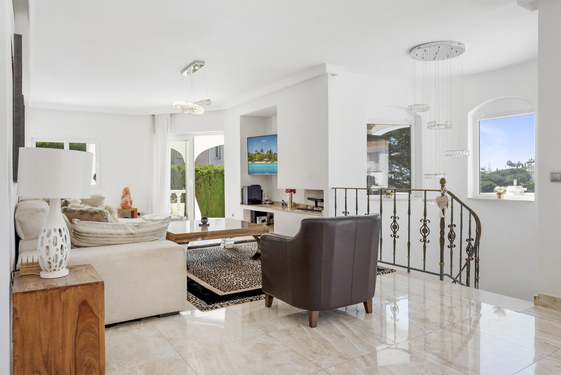 Living room with white walls, patterned rugs, a flat screen TV, and an open stairway.