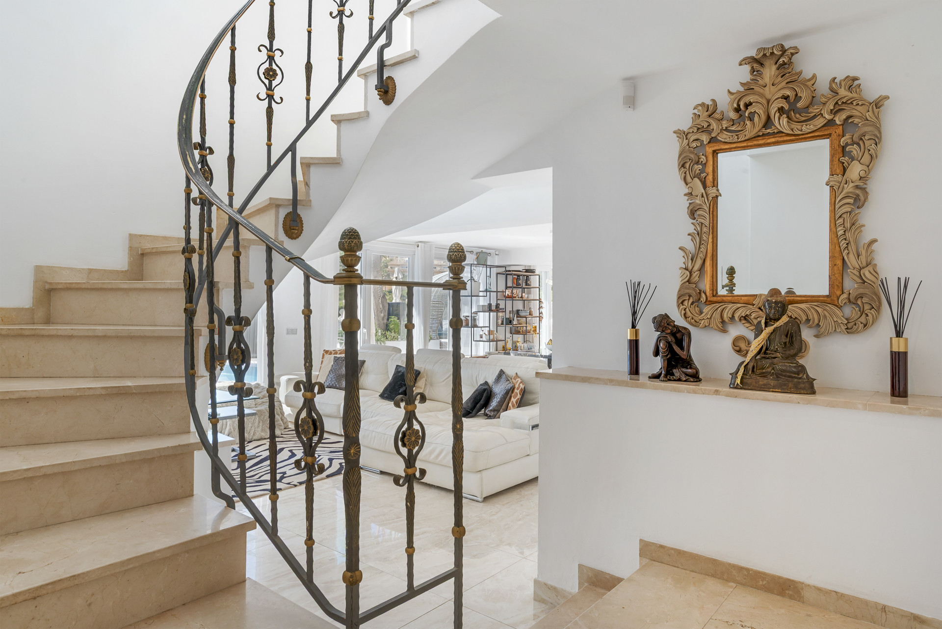 Curved marble staircase with ornate black metal railing looking into a living area.